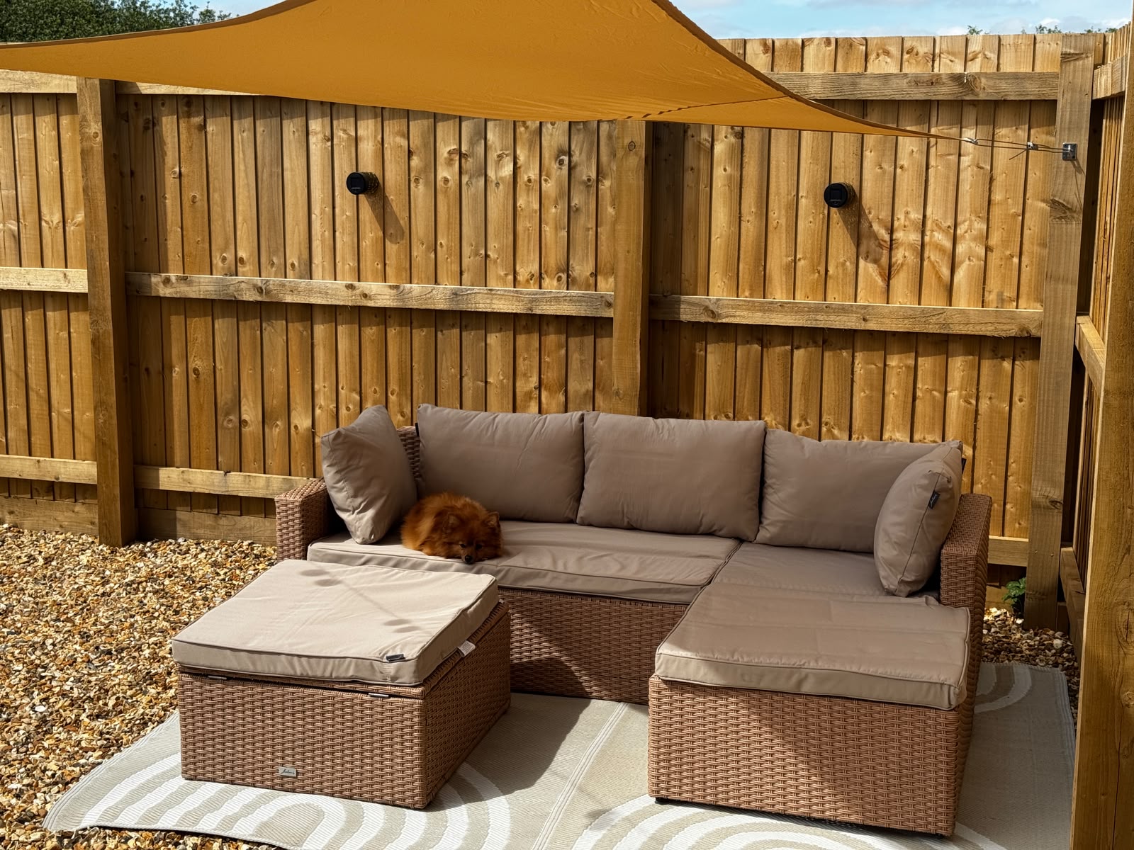 Outdoor seating area with shade sail suspended above — SPAN-KIT wire rope visible at fence fixings